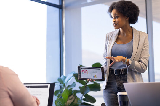 Businesswoman presenting data on tablet during casual office meeting with colleagues