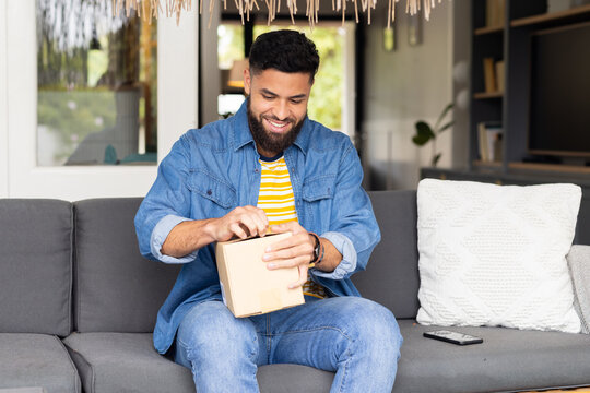 Man opening package while sitting on couch at home, smiling happily
