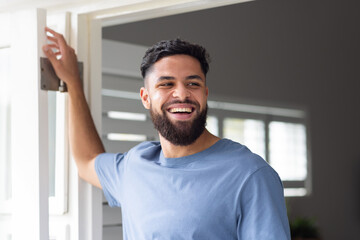 Smiling man standing at home, looking outside through open door