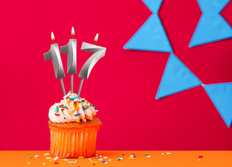 Birthday cupcake with candle number 117 on a red background with blue pennants