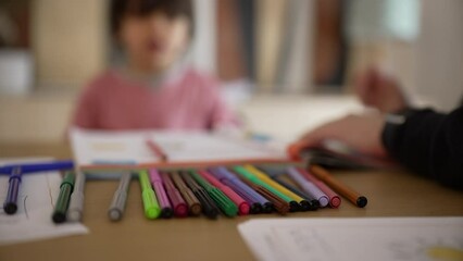 Close-up of colorful markers on a table with a blurred background of a child and parent, emphasizing creativity and educational activities in a home environment