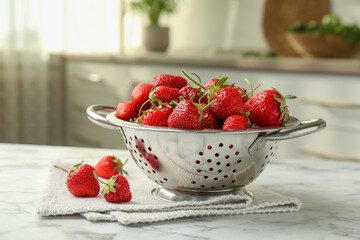 Metal colander with fresh strawberries on white marble table in kitchen