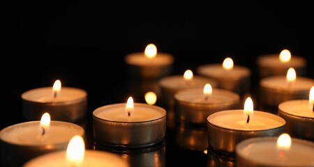 Many burning tealight candles on black background, closeup