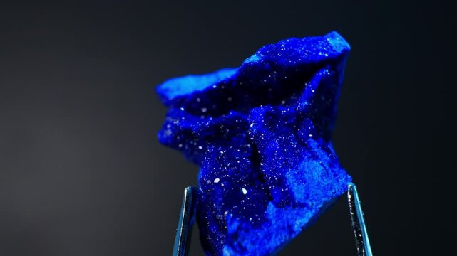 Azurite deep blue mineral from Morocco (Cu3(CO3)2(OH)2). Hardness scale: 3.5-4.5. Often used in jewelry and as art pigment. Close-up crystal formations and vibrant hues. Smooth rotation in Metal tweez