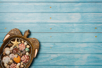 Starfish and many seashells on a decorative plate in the shape of a turtle. Blue wooden background. Top view, copy space