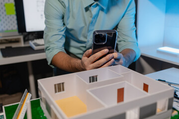 an engineer is doing a big project in the office, an architect uses electronic device to make the work he is doing easier, blueprint and model are on the desk, employee is working with concentration