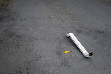 Section of white metal rain gutter downspout pipe with Phillips head screwdriver sitting on asphalt...
