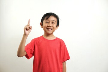 A smiling boy in a red shirt points upward with his index finger against a white background. Ideal for educational content, children's learning, and promotional materials emphasizing ideas or solution