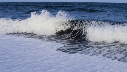 Fototapeta premium black sand beach with a foamy wave coming in to the shore and white foam on the sand