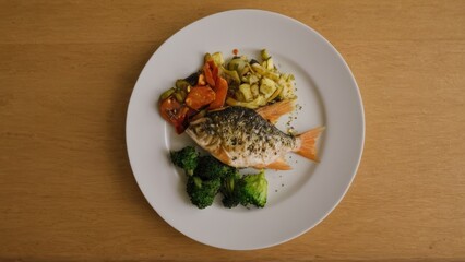 white plate topped with fish and veggies on top of a wooden table