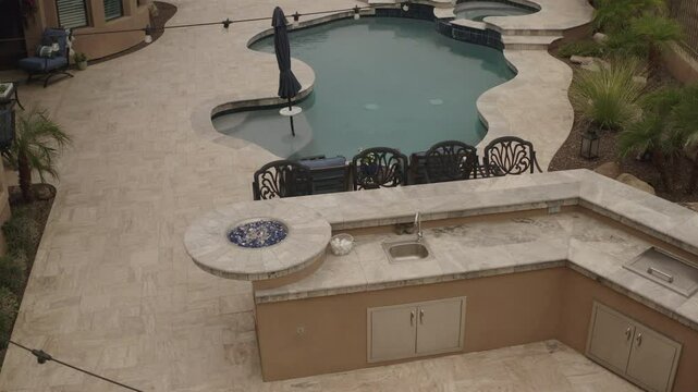 An aerial 4k video of a Deseret landscaped backyard in Arizona featuring a travertine tiled pool deck with a spa, outdoor fireplace, outdoor kitchen and putting green.