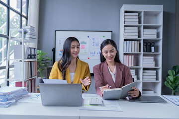 A professional photograph depicting two female entrepreneurs engaged in a collaborative discussion while diligently working in their corporate office environment.