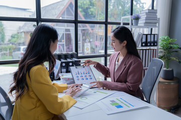 A professional photograph depicting two female entrepreneurs engaged in a collaborative discussion while diligently working in their corporate office environment.