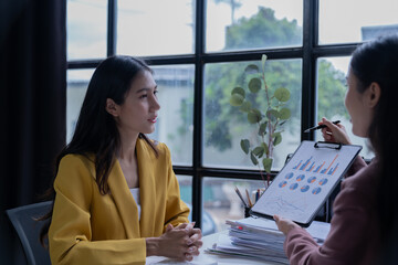 A professional photograph depicting two female entrepreneurs engaged in a collaborative discussion while diligently working in their corporate office environment.