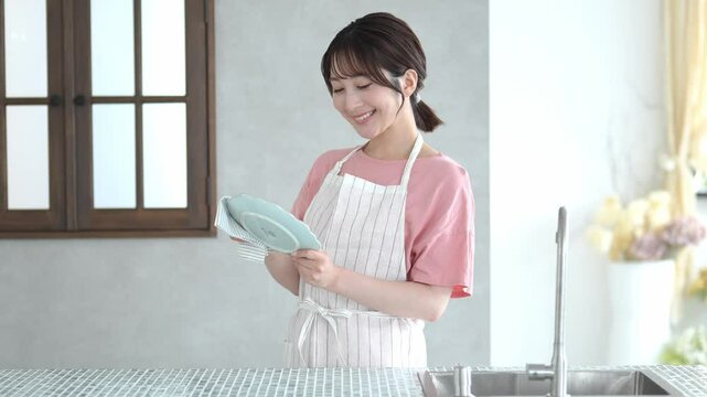 お皿を拭金ながらカメラを見る女性