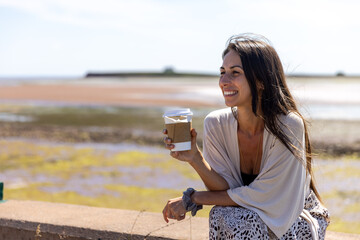 Young woman enjoying hot tea while sitting in front of ocean 