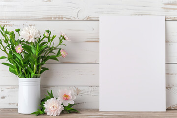 Beautiful bouquet of pink flowers in white vase next to blank canvas on rustic wooden background, perfect for greeting cards or invitations.