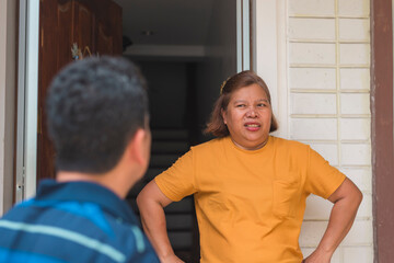 Asian woman standing at the front door sneering, feeling suspicious about her husband's late...