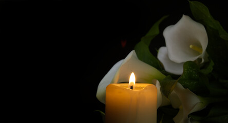Burning wax candle and white calla lily flowers in darkness