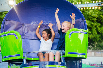 Two diverse kids riding an amusement park ride at the fun theme park. Screaming, laughing and having a great time on a thrilling carnival ride.