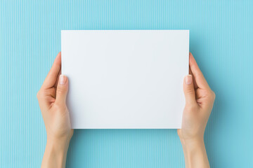 Obraz premium Hands holding a blank white paper on a blue background, perfect for mockups and presentations.
