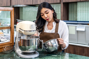 Young asian women i s shop owner Put on an apron making cream for cupcakes, Using electric mixer,...