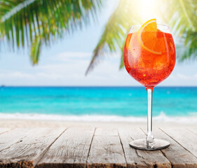 Glass of Aperol Spritz on a table with a stunning sea and beach background