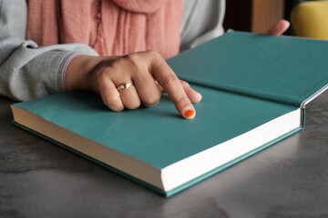 Close-up of a person's hand pointing to a book page with a finger, focus on the orange nail polish