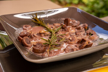 Roast lamb kidneys in red wine cream sauce and a sprig of rosemary served on a brown plate