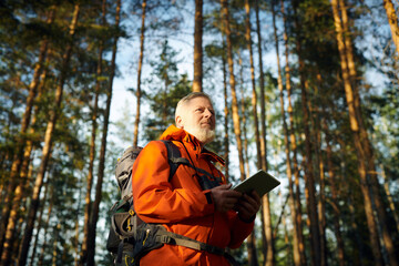 Low angle view of senior Caucasian male tourist wearing orange jacket using digital tablet while...