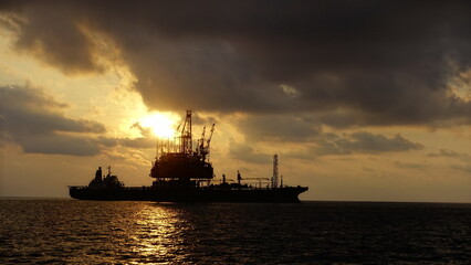 Drilling rig and FPSO ship or floating processing storage offloading ship silhouette view in sunset offshore background