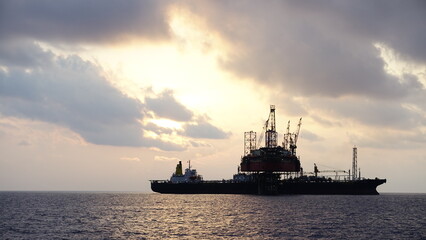Drilling rig and FPSO ship or floating processing storage offloading ship silhouette view in sunset offshore background
