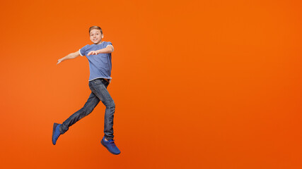 Cute carefree boy dancing, jumping in air, having fun on orange background
