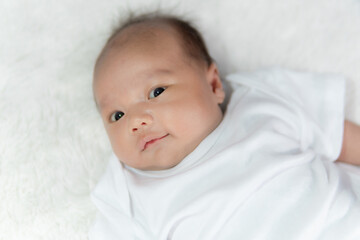 Close-up of a happy smiling baby on a white cotton bed in a bright bedroom.