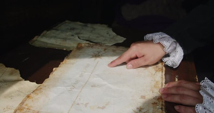 Amazing slow motion cinematic shot of the finger of a person dressed in medieval clothing inside a ship's structure pointing out places on an ancient map of America.