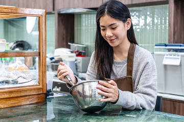 Young asian women is shop owner Put on an apron making cream for cupcakes, Using electric mixer,...