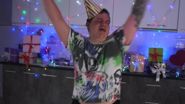 House party with emotionally dancing man who's had too much to drink waving his arms amid festive kitchen decorations. Slow motion.