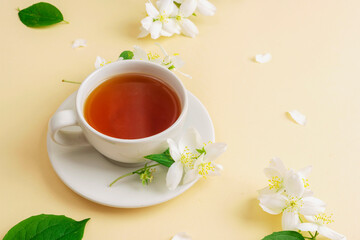 A cup of tea and jasmine flowers on beige background. Top view, copy space