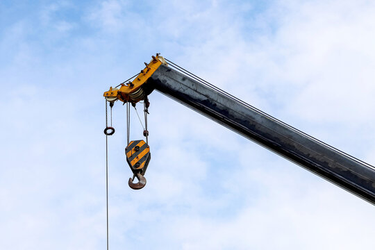 Closeup of an old lifting hook attached to sheave suspended by wire rope from boom of crane against the sky