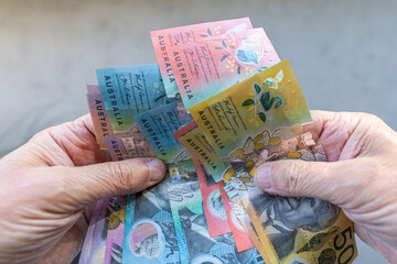 Close-up of a man counting Australian dollars banknotes on his hands, against plain background.