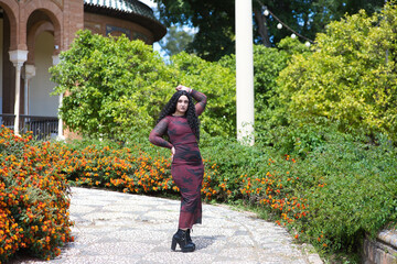 Fototapeta premium young and beautiful latin woman, brunette with curly hair, walks among the vegetation and buildings of a famous park in spain. The woman is on holiday in seville and enjoys the sunshine.
