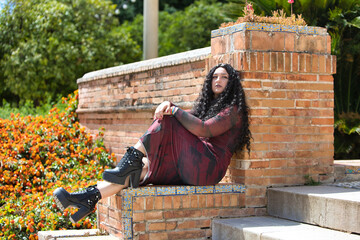 Latin woman, brunette with curly hair, young and beautiful sitting on the stairs in a city park....
