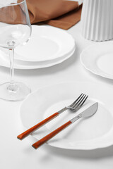 Stylish table setting with white dishware on white tablecloth