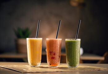 Three different refreshing smoothies with black straws sitting on wooden table 