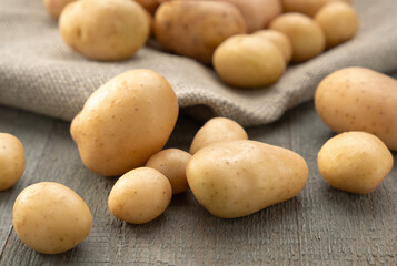 Young clean potatoes lie scattered on a wooden background with jute cloth, bag