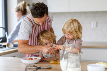 Young nuclear family making pancakes together. Parents and children in kitchen, preparing pancake...