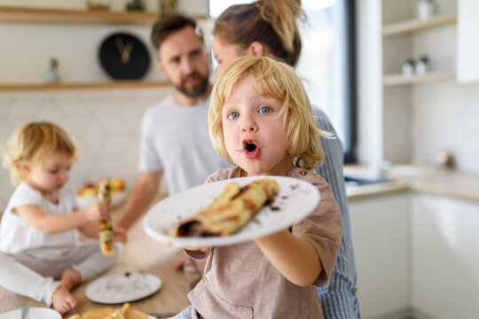 Young nuclear family making pancakes together. Parents and children in kitchen, spending weekend day indoors. - Powered by Adobe