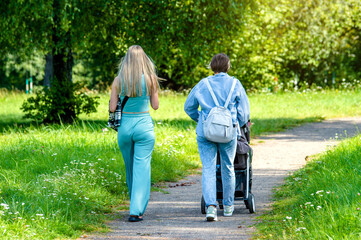 Obraz premium Two girls with a baby stroller are walking in the summer park 
