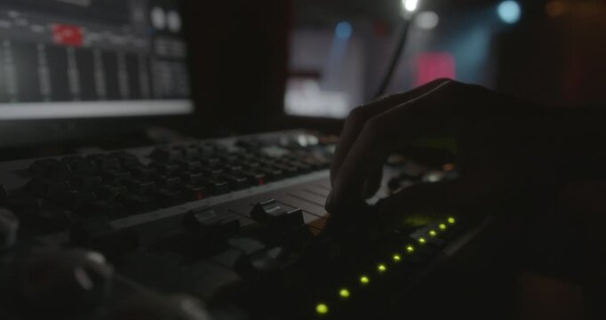 Amazing slow motion shot of the detail of a hand of a live show sound engineer moving a fade of the sound table moving the stage lights.