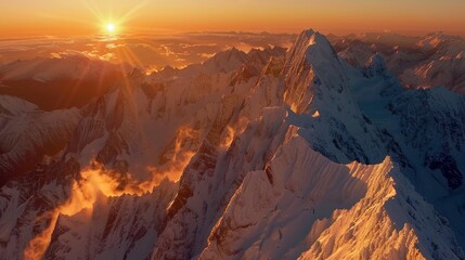 Naklejka premium A breathtaking aerial view of snow-covered mountain ranges at sunset, with a golden hue spreading across the peaks and clouds creating a dramatic scene.